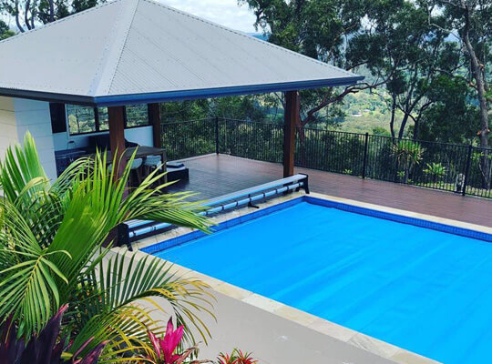Sunbather Thermal Cover - 2mm Mid Blue A backyard with a swimming pool cover over a underground pool.